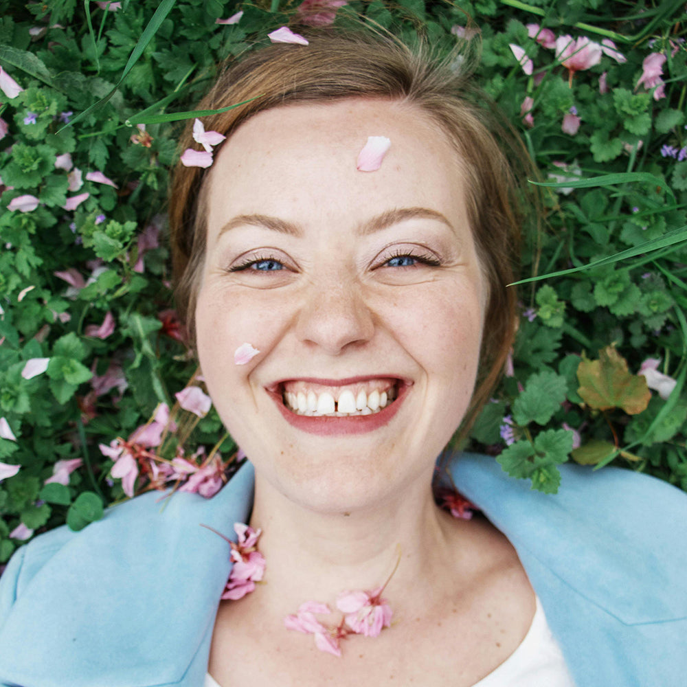 Calcium Carbonate works to gently polish away surface stains and discoloration, revealing a brighter, whiter smile, like for this woman laying in a bed of flowers